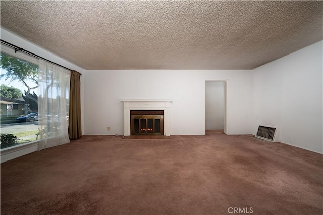 unfurnished living room featuring a textured ceiling, carpet, a fireplace with flush hearth, and visible vents