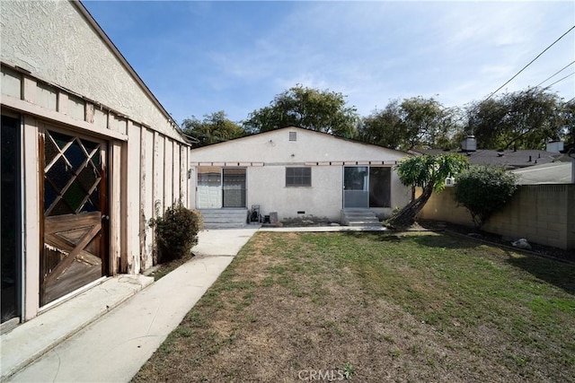 back of house featuring entry steps, fence, a lawn, and stucco siding