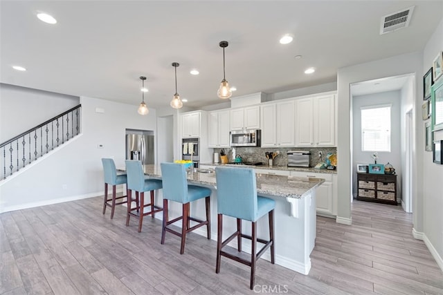 kitchen with light stone counters, a kitchen island with sink, stainless steel appliances, white cabinetry, and pendant lighting