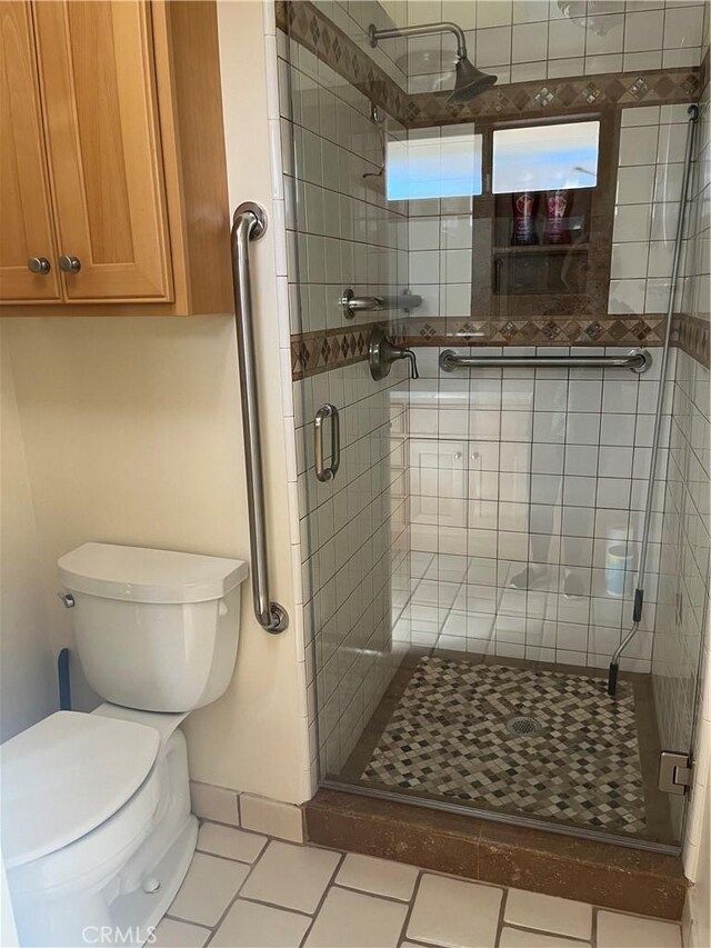 bathroom featuring a stall shower, tile patterned flooring, baseboards, and toilet