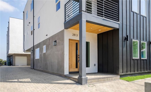 entrance to property featuring board and batten siding, decorative driveway, and stucco siding