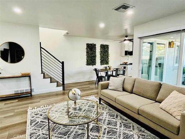 living area featuring light wood finished floors, visible vents, ceiling fan, and stairs