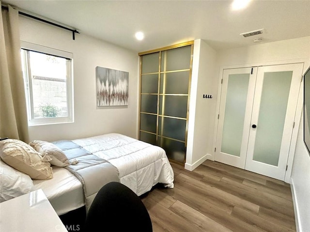 bedroom with wood finished floors, a closet, visible vents, baseboards, and recessed lighting