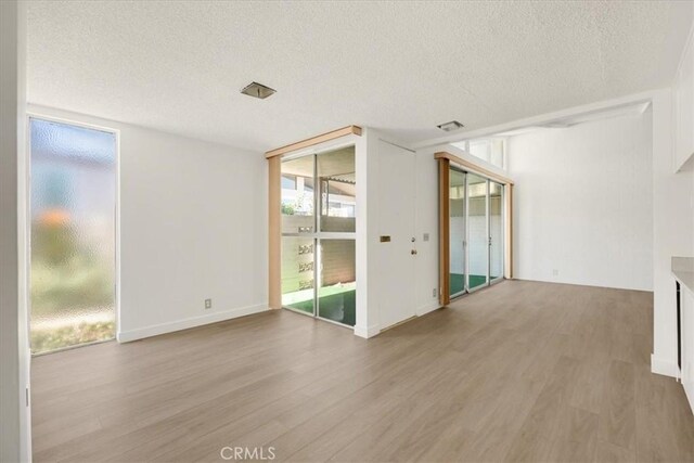 unfurnished room with a wall of windows, visible vents, light wood-style flooring, and a textured ceiling