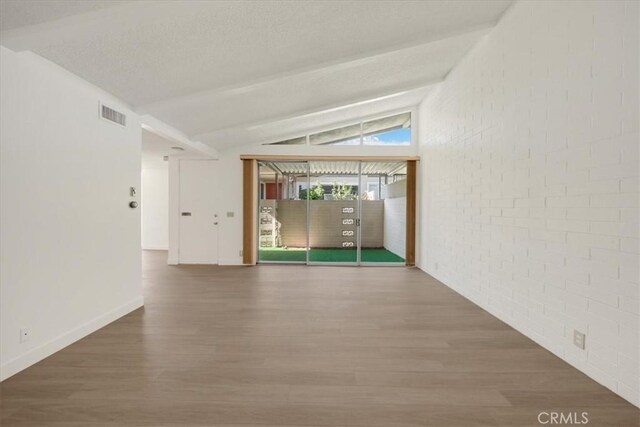 empty room featuring baseboards, visible vents, lofted ceiling with beams, brick wall, and wood finished floors