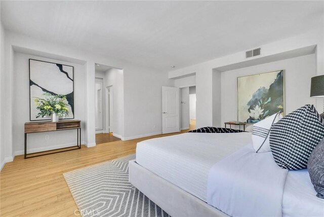 bedroom with baseboards, visible vents, and wood finished floors