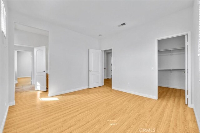 unfurnished bedroom with light wood finished floors, visible vents, baseboards, a walk in closet, and a closet