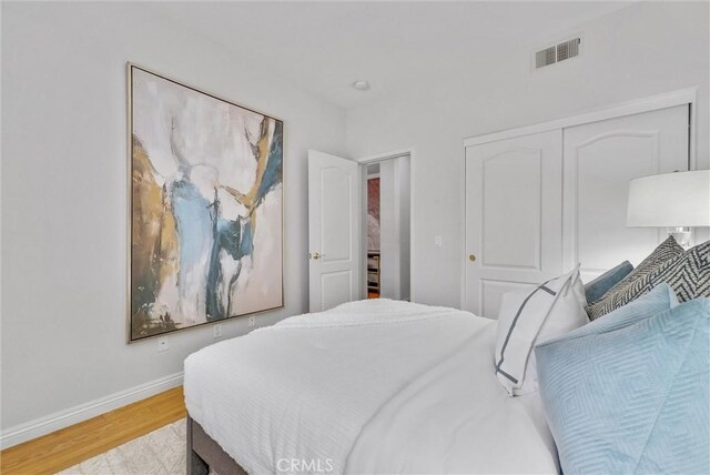 bedroom with light wood-type flooring, baseboards, visible vents, and a closet