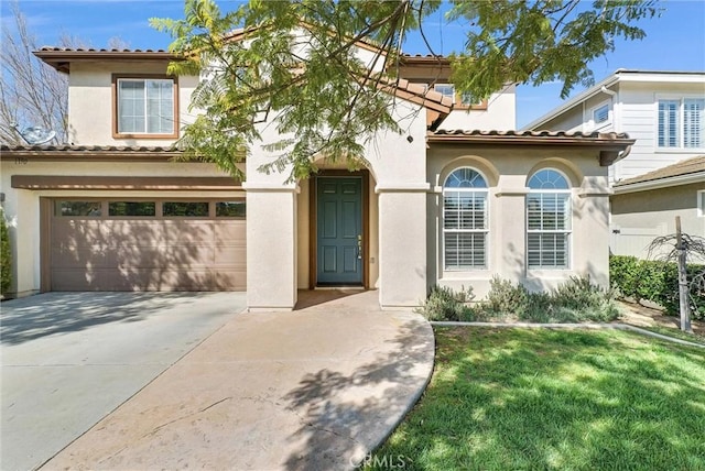 mediterranean / spanish-style home with an attached garage, driveway, a tiled roof, stucco siding, and a front lawn