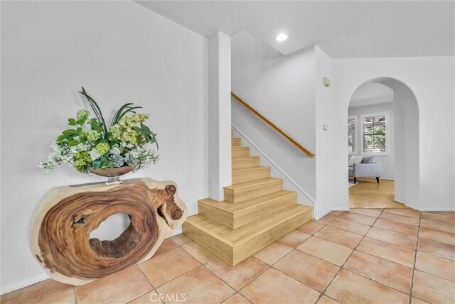 stairway featuring tile patterned flooring, arched walkways, baseboards, and recessed lighting