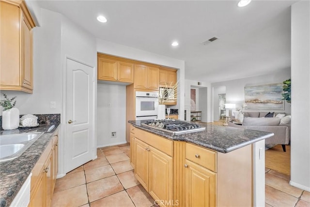 kitchen featuring visible vents, open floor plan, light brown cabinets, dark stone countertops, and white appliances