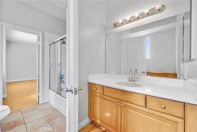 bathroom featuring tile patterned flooring, enclosed tub / shower combo, vanity, and toilet