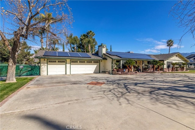 single story home with an attached garage, driveway, fence, and solar panels