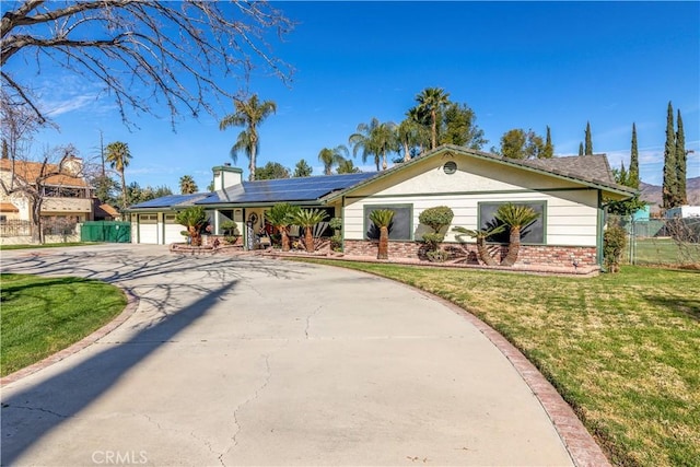 ranch-style home with a garage, brick siding, driveway, roof mounted solar panels, and a front yard