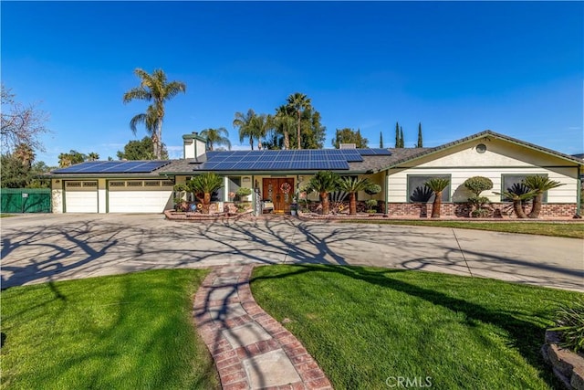 ranch-style house with a front yard, roof mounted solar panels, an attached garage, and concrete driveway