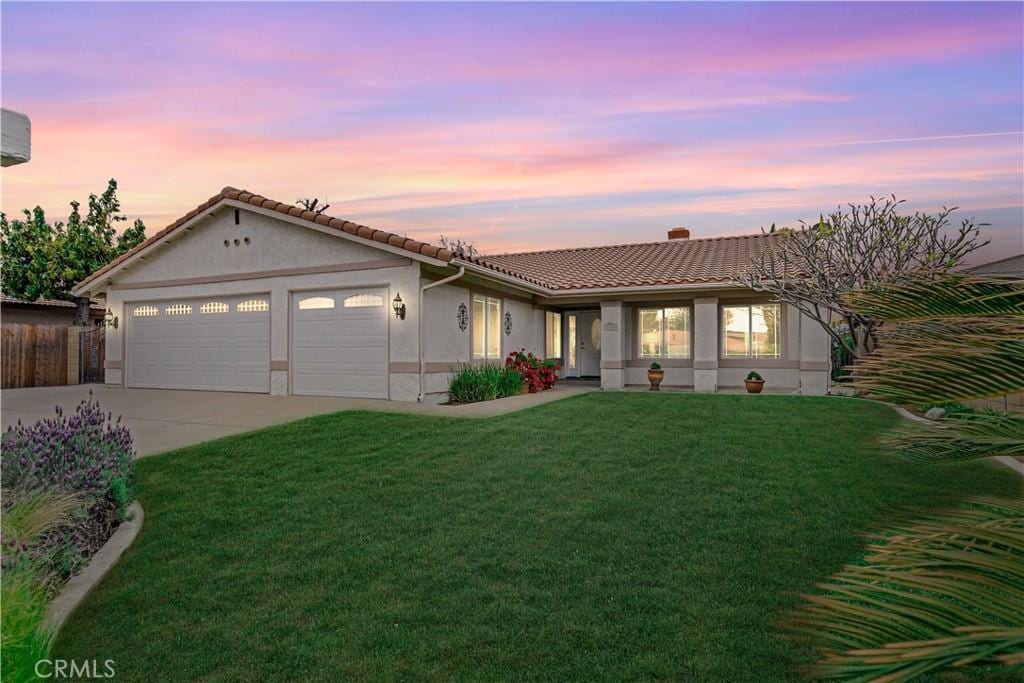 single story home with a tile roof, concrete driveway, stucco siding, an attached garage, and a yard
