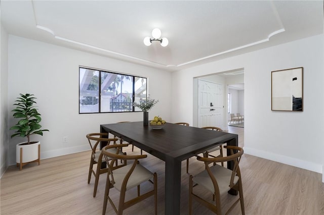 dining room with a raised ceiling, baseboards, and light wood finished floors