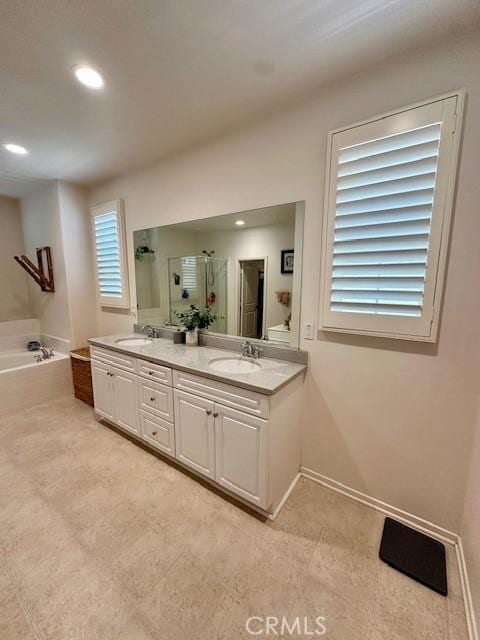 bathroom with double vanity, a stall shower, baseboards, a bath, and a sink