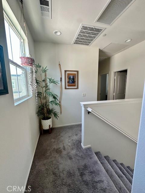 corridor featuring dark colored carpet, visible vents, and baseboards