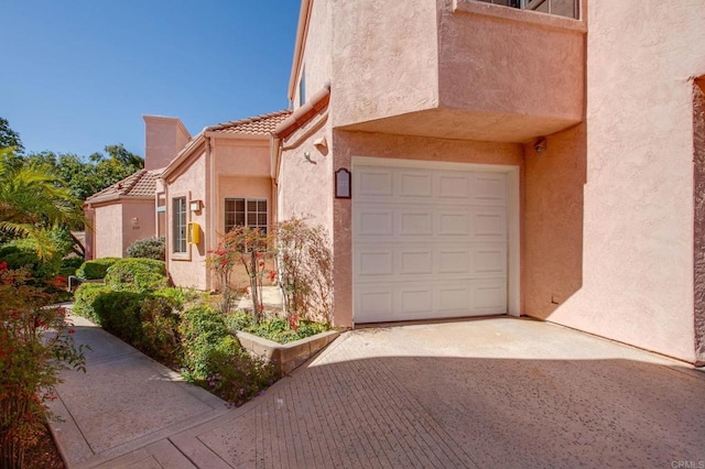 exterior space featuring a garage, a tiled roof, and stucco siding