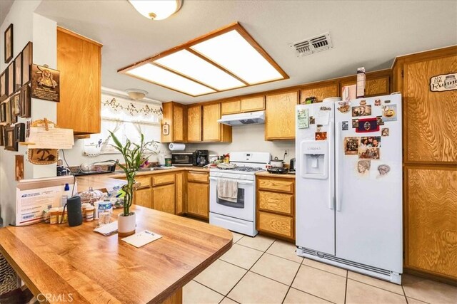 kitchen with white appliances, brown cabinets, visible vents, and under cabinet range hood