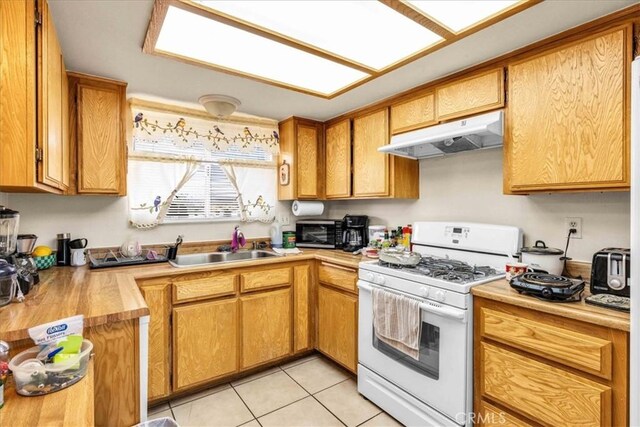 kitchen with light tile patterned floors, under cabinet range hood, a sink, light countertops, and white gas range oven