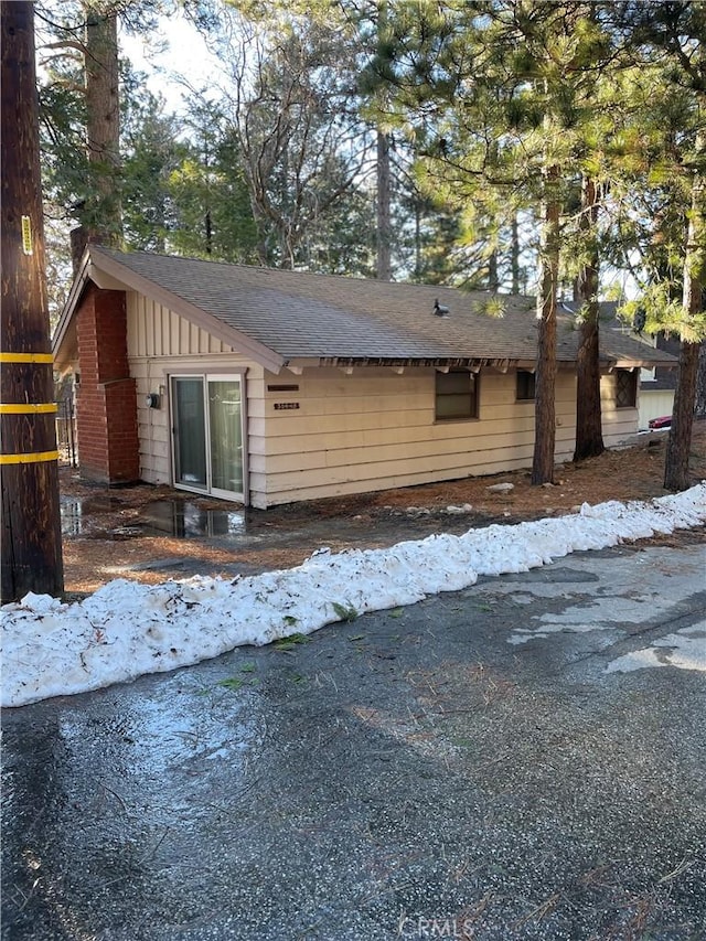 view of side of property with a shingled roof, board and batten siding, and brick siding