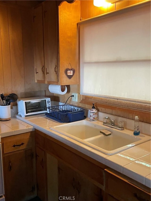 kitchen featuring tile countertops, a toaster, a sink, and brown cabinets