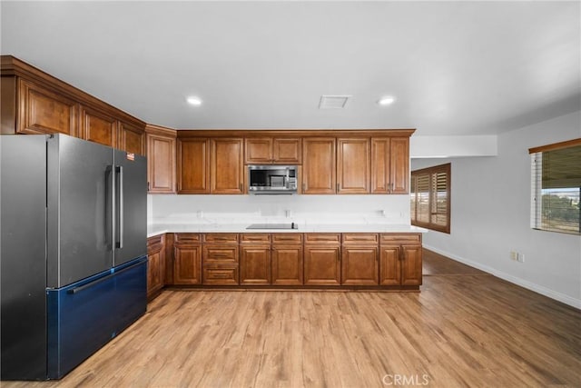 kitchen featuring light countertops, stainless steel microwave, brown cabinetry, freestanding refrigerator, and light wood-style floors