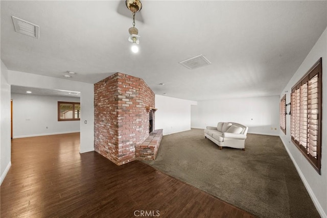 unfurnished living room featuring a brick fireplace, visible vents, dark wood finished floors, and baseboards