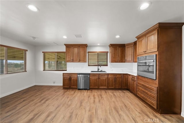 kitchen featuring appliances with stainless steel finishes, brown cabinets, light countertops, light wood-style floors, and a sink