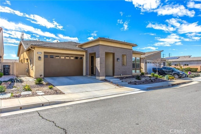 prairie-style home featuring a garage, concrete driveway, fence, and stucco siding