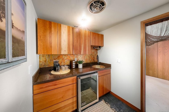 kitchen featuring wine cooler, dark countertops, visible vents, brown cabinetry, and a sink