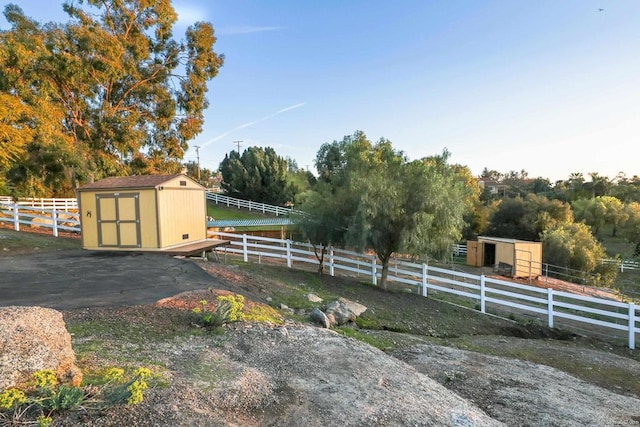 view of yard with a rural view, a storage unit, fence, and an outbuilding