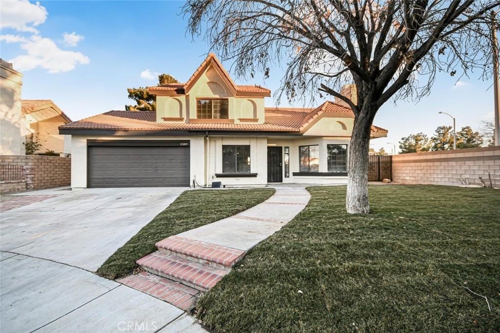 mediterranean / spanish-style home featuring fence, driveway, a tiled roof, stucco siding, and a front lawn