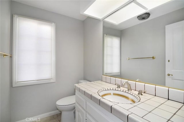 half bathroom featuring tile patterned floors, toilet, vanity, a skylight, and baseboards