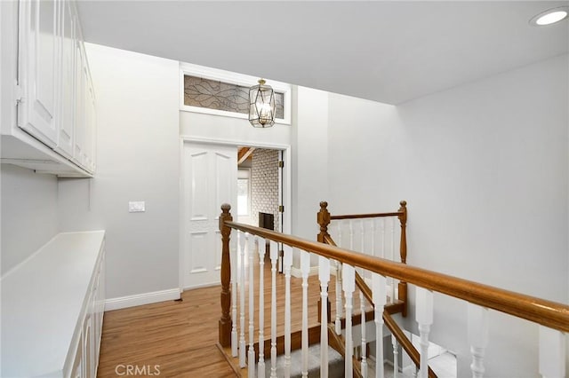 hall with recessed lighting, light wood-style flooring, baseboards, and an upstairs landing