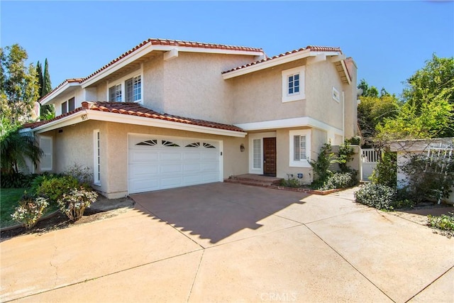 mediterranean / spanish-style home with an attached garage, a tiled roof, concrete driveway, and stucco siding