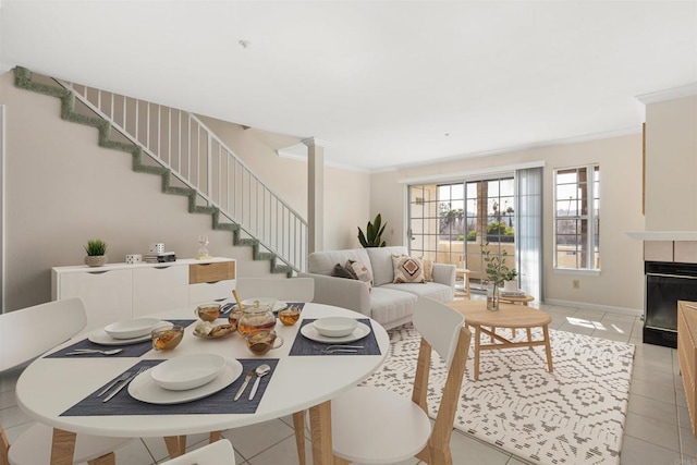 dining space with crown molding, a fireplace, stairway, light tile patterned flooring, and baseboards