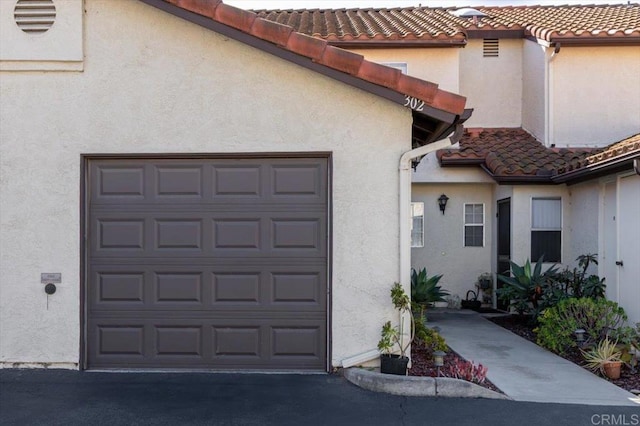 property entrance with a garage, a tile roof, and stucco siding