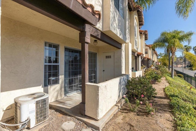 doorway to property with central AC, fence, and stucco siding