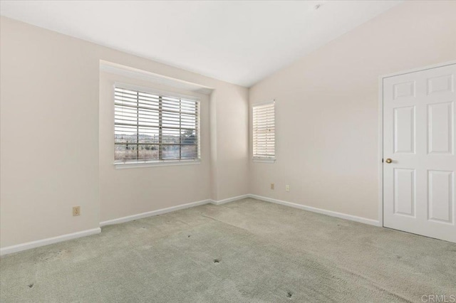 spare room featuring light carpet, lofted ceiling, and baseboards