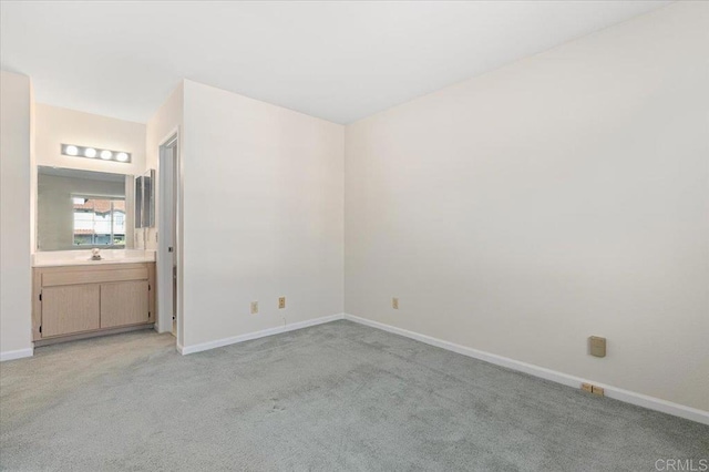 unfurnished bedroom featuring light carpet, a sink, ensuite bath, and baseboards