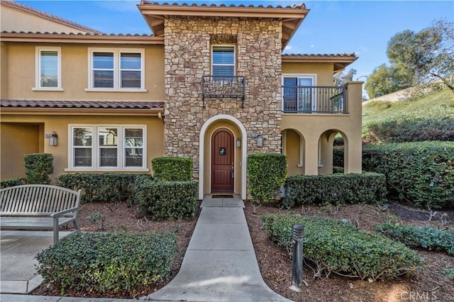 mediterranean / spanish house featuring a balcony, stone siding, and stucco siding