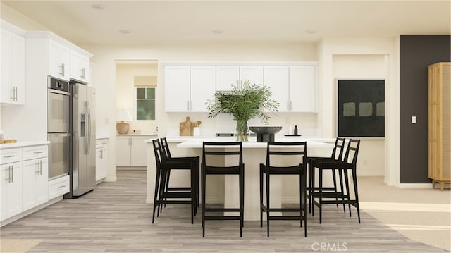 kitchen with light countertops, appliances with stainless steel finishes, white cabinets, light wood-type flooring, and a kitchen bar