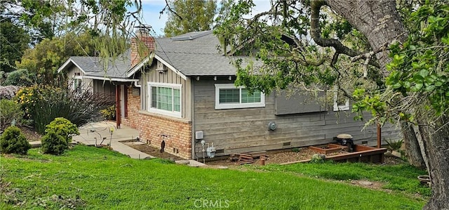 view of side of home with a yard, board and batten siding, crawl space, brick siding, and a chimney