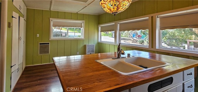 kitchen with a sink, wood counters, heating unit, dark wood finished floors, and white cabinetry