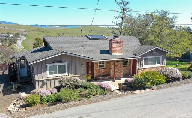 view of front of home with brick siding, board and batten siding, a chimney, and roof with shingles