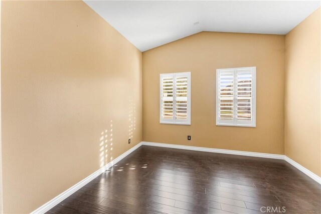 empty room featuring vaulted ceiling, dark wood-style flooring, and baseboards