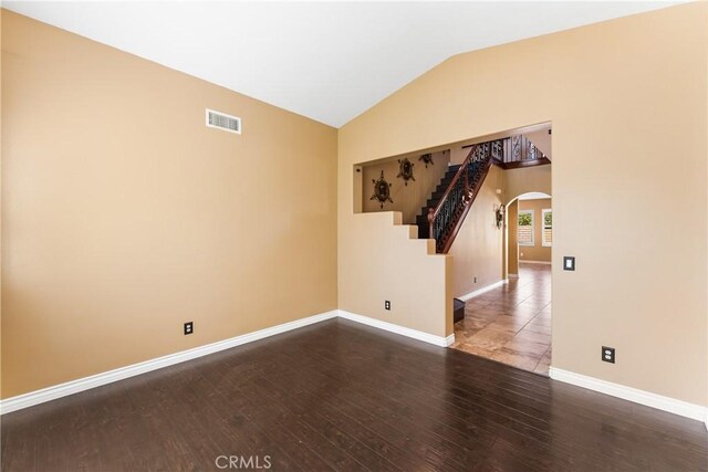 empty room featuring arched walkways, wood finished floors, visible vents, baseboards, and vaulted ceiling